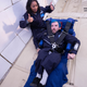 Eric Ingram, a returning flyer from AstroAccess’s inaugural 2021 mission, practices getting in and out of a 5-point harness attached to a simulated space capsule seat. He is joined by astronaut and aerospace executive Sirisha Bandla.